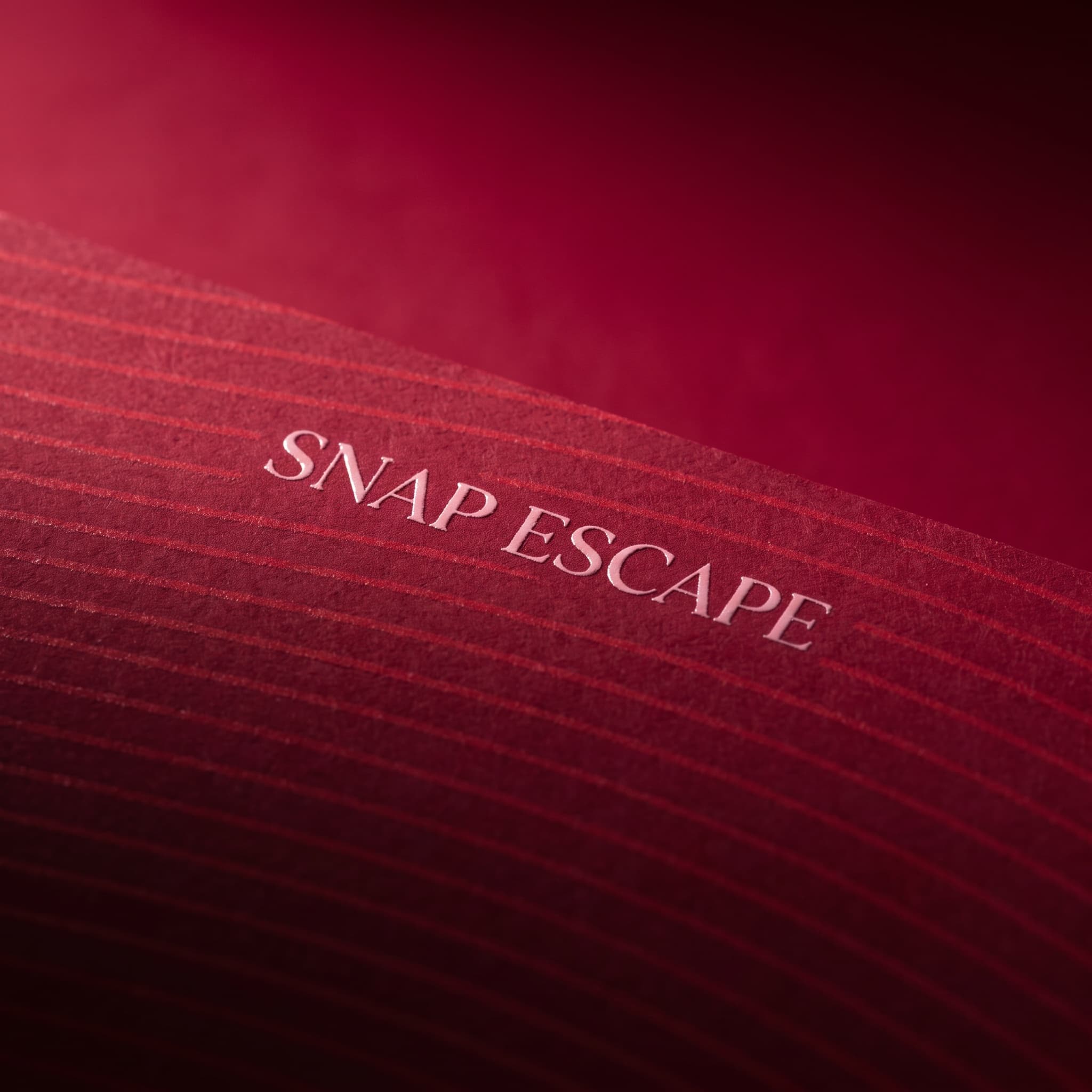 Extreme close-up of red ribbed card, the words Snap Escape picked out in pale foil.